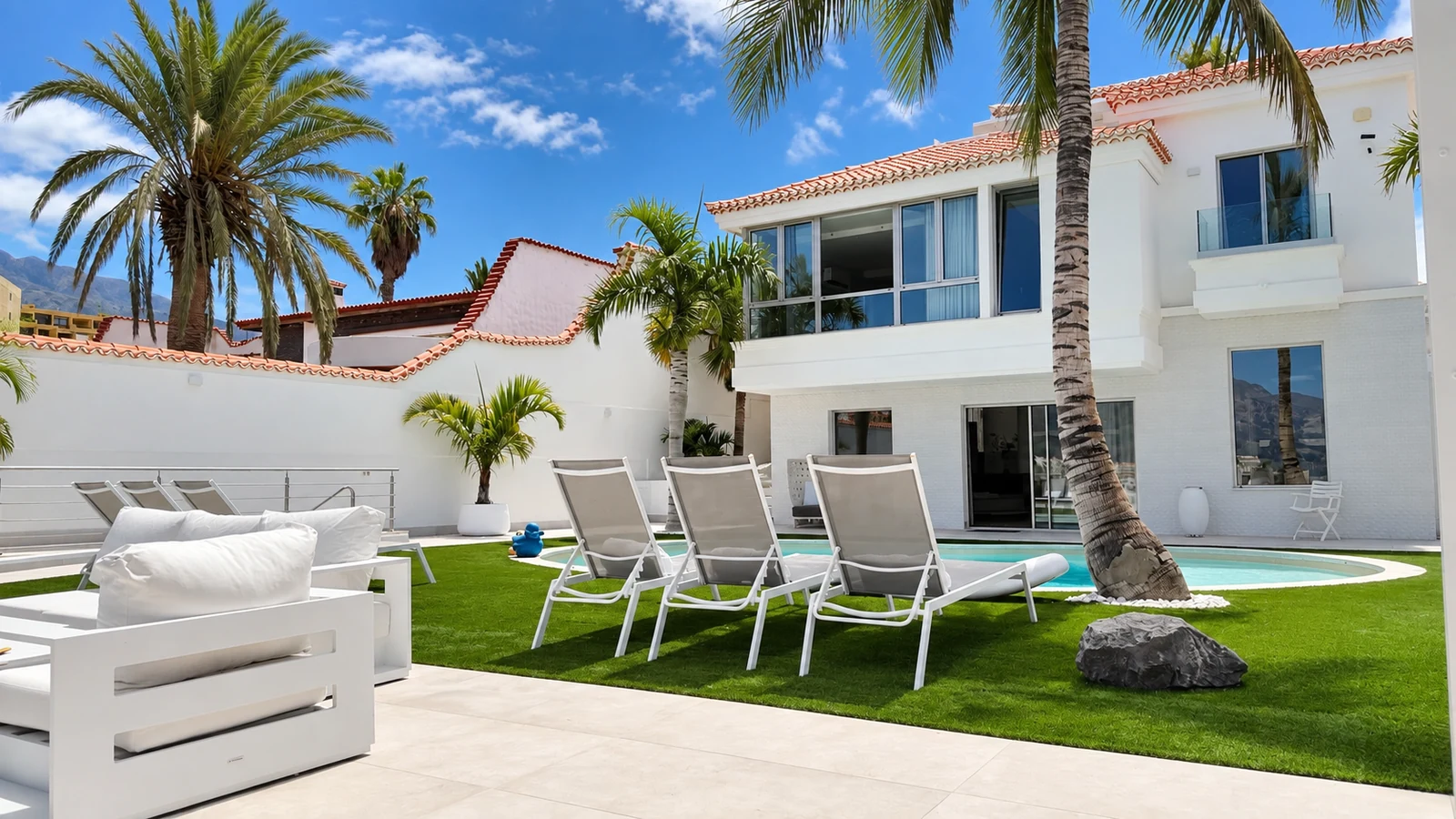 Pool courtyard with lawn, palm trees and sun loungers at Villa White Octopus, Tenerife